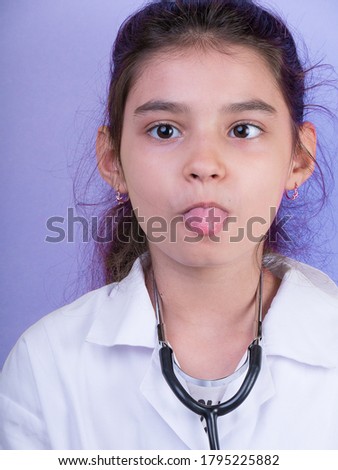 Little funny girl with a collorful stethoscope while wearing Doctor's uniform. Excitement and fascination concept. Coronavirus background. foolish grimaces comical crazy gestur.  Funny . tongue