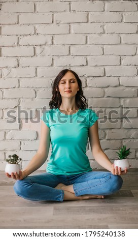 A young girl is sitting on the floor in a yoga and meditation pose holding indoor plants in her hands.