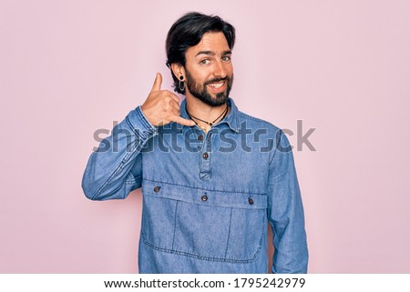 Young handsome hispanic bohemian man wearing hippie style over pink background smiling doing phone gesture with hand and fingers like talking on the telephone. Communicating concepts.