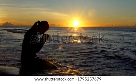 Silhouette of woman kneeling and praying over beautiful sunrise at sea background Royalty-Free Stock Photo #1795257679