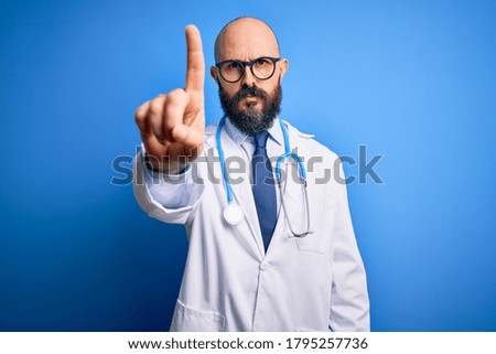 Handsome bald doctor man with beard wearing glasses and stethoscope over blue background Pointing with finger up and angry expression, showing no gesture