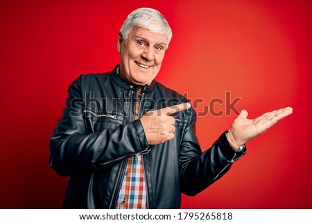 Senior handsome hoary man wearing casual shirt and jacket over isolated red background amazed and smiling to the camera while presenting with hand and pointing with finger.