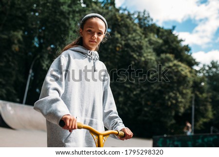 City portrait of handsome girl kid wearing gray blank hoodie or sweatshirt with space for your logo or design. Mock up for print. A girl on a scooter in skate park. Healthy lifestyle and sport concept