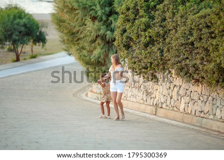 Portrait of a young beautiful girl and Mom on the beach with a baby in her arms in stylish fashionable clothes. Walk on the weekend enjoying their vacation.