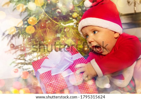 Happy little toddler baby boy with scream holding New Year present in front of Christmas tree