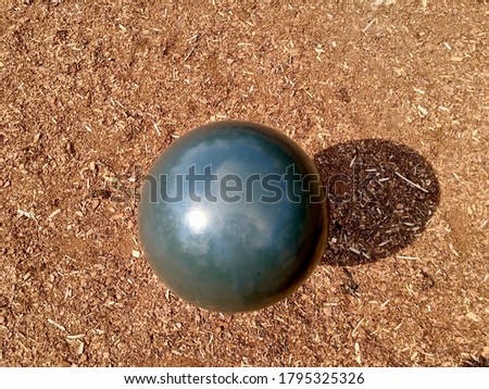 A big black round plastic ball at a playground. A dark shadow against a brown wood like background, outdoors. Photo from above makes a cool and artful view.