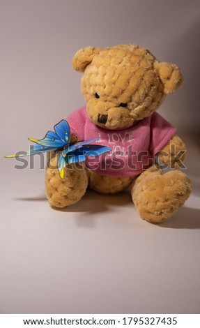 a beautiful picture of a toy that is a yellow bear in a pink shirt with a blue butterfly on its paw