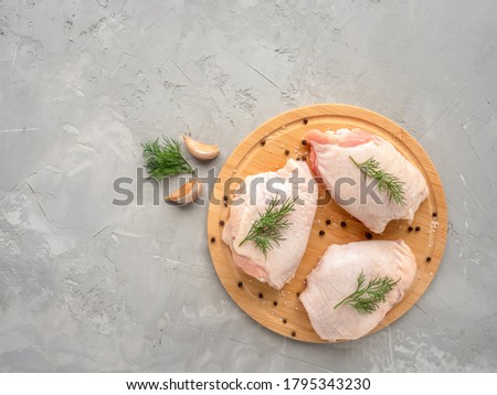 Raw chicken thighs on cutting board with ingredients for cooking at grey concrete kitchen table. Top view with copy space. Royalty-Free Stock Photo #1795343230