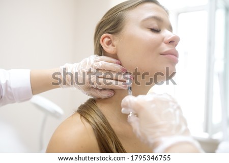 The beautician gives the patient injections in the lip area during the procedure for correcting the angles of the lower jaw with a filler
 Royalty-Free Stock Photo #1795346755