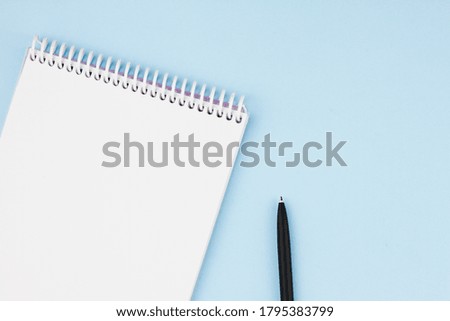 White blank notebook with a black branded pen on a light blue background. View from above. Place for your text. Photo concept.