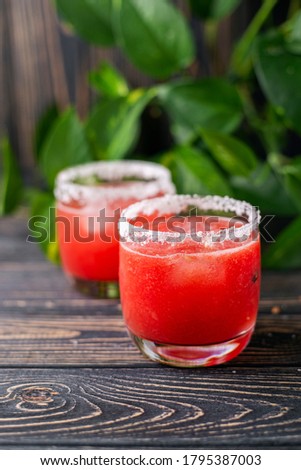 Refreshing cold juice drink - freshly squeezed watermelon lemonade with ice. Bright juicy red non-alcoholic cocktail on a dark wooden background. Idea for a homemade drink recipe. Selective focus.