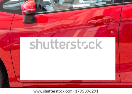Horizontal close-up shot of a blank white sign on a red car door.