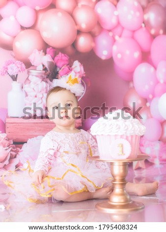 Baby girl wearing pink with birthday cake on a smash the cake photo session with pink balloons
