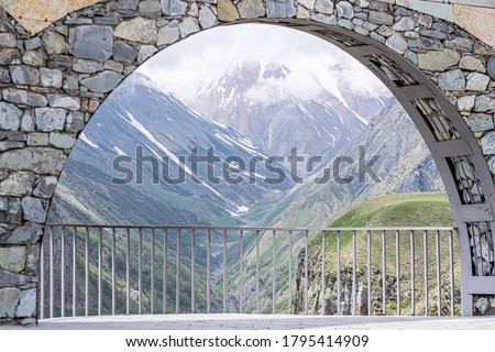 Gudauri view point monument arch with bars and framed dramatic Kazbegi national park mountains. Adventure in Georgia.
