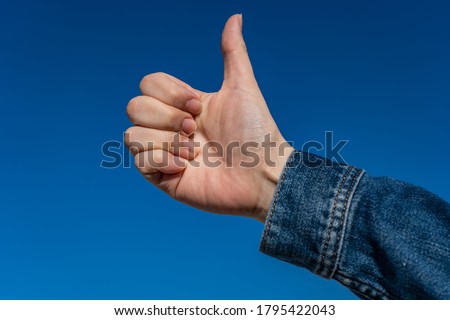 Hand in denim doing ok sign at the sky
