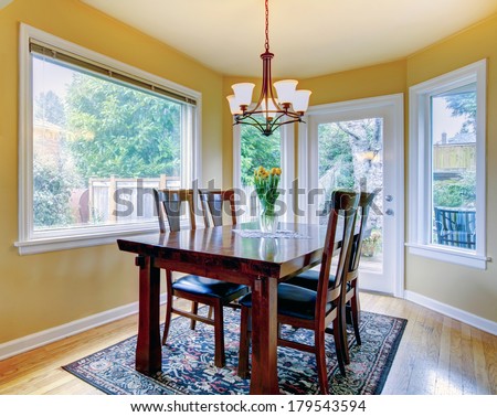 Yellow wall small dining room with hardwood floor and rug. Furnished with wooden table set. Decorated with fresh flowers