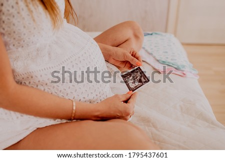 Pregnant woman looking at her baby twins sonography. Happy expectant lady enjoying first photo of her kids, face is unrecognizable