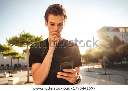 Serious young man looking at mobile phone on sunny day in city. High quality photo