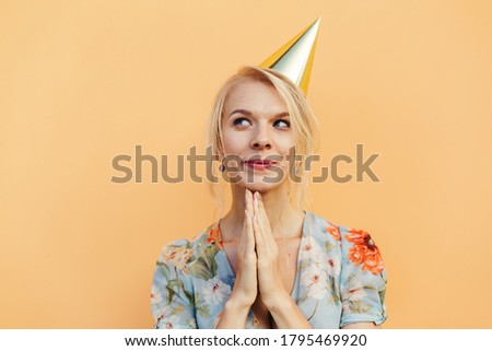 Image of beautiful cute woman in party cone posing isolated over orange pastel background.