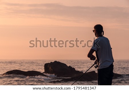 Silhouette of a young man fishing, spining style, from the rocks at the galician coast, in front of the Atlantic Ocean while the sun goes down. Magic moment to get better fishes