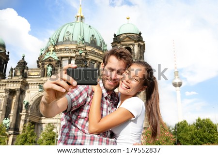 Travel couple selfie self portrait, Berlin, Germany. Happy tourists people in front of Berlin Cathedral / Berliner Dom with Fernsehturm / Berlin TV Tower in the background. Asian woman, Caucasian man.