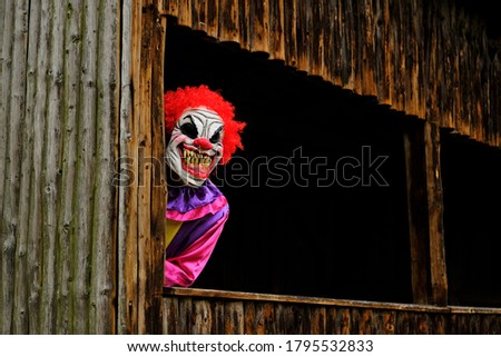 Halloween holiday. Creepy clown costume. Spooky clown in a bright overalls in an old wooden hut.Autumn holidays in October. Festival and carnival . Horror and fear.Autumn seasonal holiday