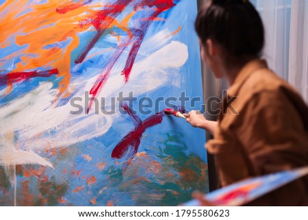 Young artist in art workshop using red paint on large canvas to create a contemporary painting. Modern artwork paint on canvas, creative, contemporary and successful fine art artist drawing