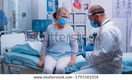 Retired old woman wearing protection mask signing for discharge. Modern private hospital or clinic. Healthcare medical physician consultation during COVID-19 global crisis, healthcare problem