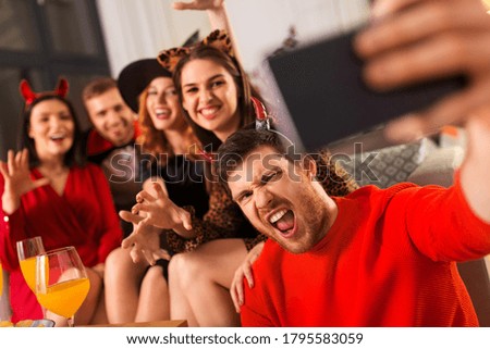 friendship, holiday and people concept - group of happy smiling friends in halloween costumes of vampire, devil, witch and cheetah taking selfie by smartphone at home party at night