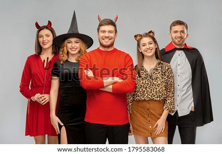 friendship, holiday and people concept - group of happy smiling friends in halloween costumes of vampire, devil, witch and leopard over grey background