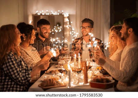 holidays, celebration and people concept - happy friends with sparklers having christmas dinner at home Royalty-Free Stock Photo #1795583530