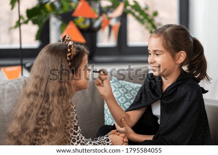 halloween, holiday and childhood concept - smiling little girls in party costumes doing face painting at home
