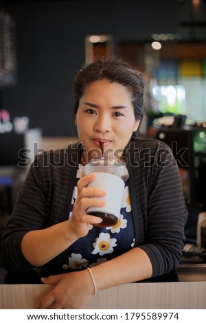 A picture of a middle-aged woman drinking coffee through a straw from a plastic cup in her hand.  At one of the coffee shops happily on vacation