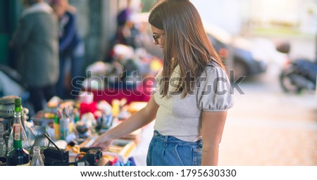 Young beautiful woman smiling happy and confident. Standing with smile on face looking a jumble sale at the town street