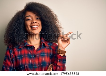 Young beautiful african american woman wearing casual shirt over isolated background with a big smile on face, pointing with hand and finger to the side looking at the camera.