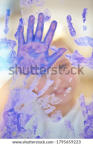Happy child paints many handprints by hand on a window