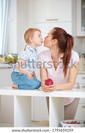 Happy mother and little daughter kiss in the kitchen
