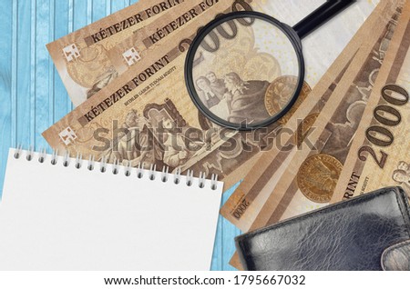 2000 Hungarian forint bills and magnifying glass with black purse and notepad. Concept of counterfeit money. Search for differences in details on money bills to detect fake