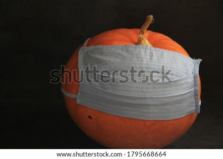 pumpkin in a medical mask on a dark background. halloween. coronavirus. pandemic, quarantine. vegetables, autumn season. 
