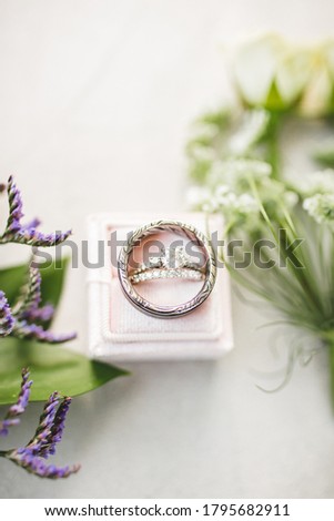 Pictures of a man and woman wedding rings on a pink ring box with some floral accents. Beautiful white gold diamond engagement ring, diamond wedding band and titanium mens ring