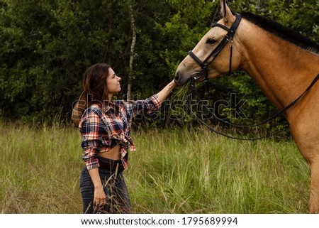 Beautiful young woman walking with brown horse on green field