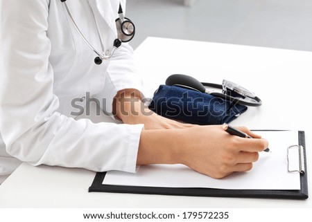 Female physician writing medical notes on clipboard