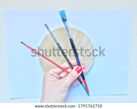 Red nail polish hand holding colorful watercolor brushes.