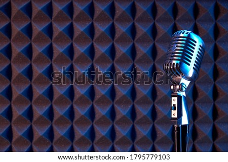 Studio retro condenser microphone on acoustic foam panel background with blue side light