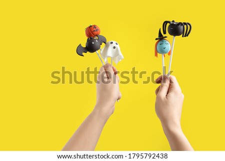 Woman with delicious cake pops on yellow background, closeup. Halloween celebration