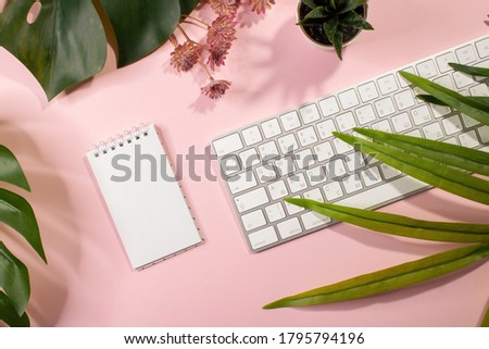 Flat lay of empty notepad, keyboard and palm leaves on pink background