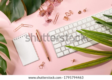 Flat lay of empty notepad, keyboard, golden office supplies and palm leaves on pink background