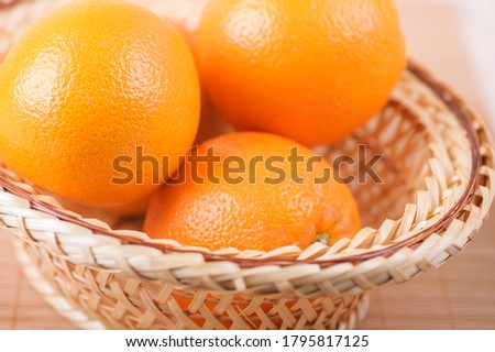 Three big oranges in a wicker basket on bamboo table cloth.