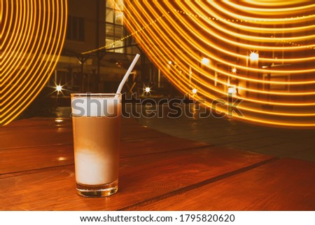 A glass of coffee with a straw, outside, toned photo.