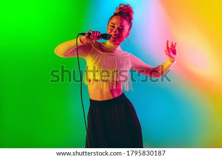 Young musician playing, singing on gradient background in neon. Music
